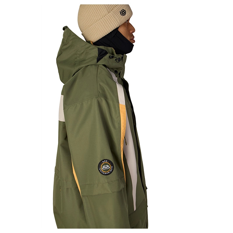 A side profile of a person wearing a green hooded jacket with cream and yellow panels, a beige knit beanie, and a black face mask, against a plain white background.