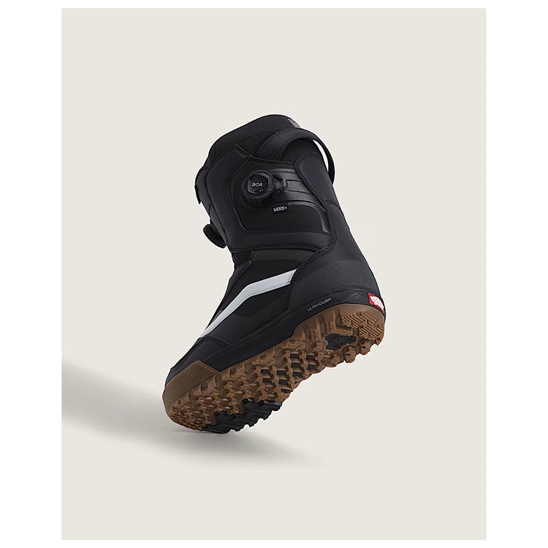 A single black snowboard boot with a brown gum sole, featuring a white stripe and a dial closure system, shown floating against a light beige background.