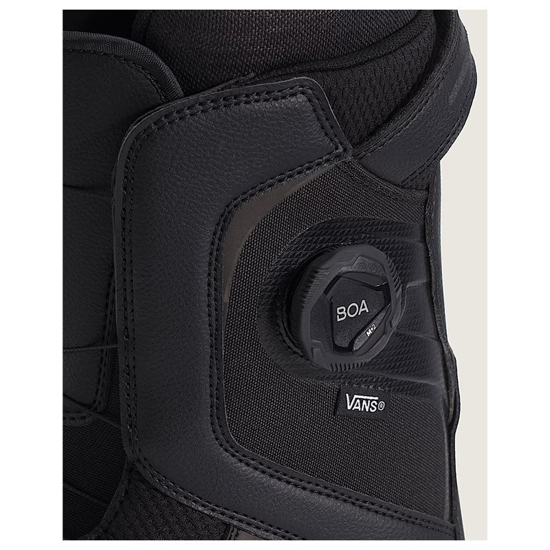 Close-up of a black Vans snowboard boot featuring a BOA dial closure system and the Vans logo, set against a light off-white background.