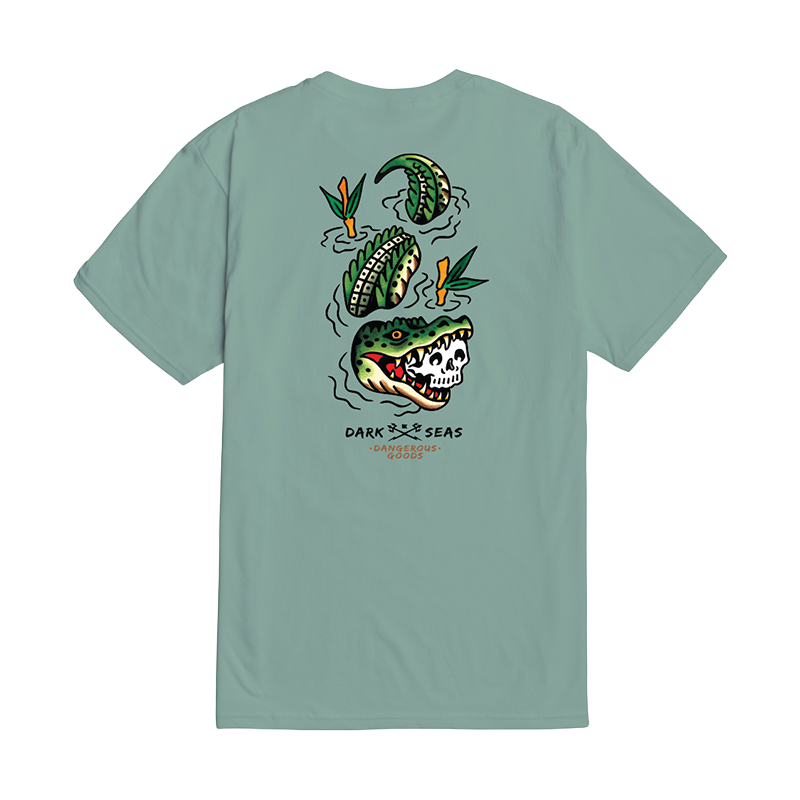 A sage green short-sleeve t-shirt shown from the back, featuring a graphic of a skull-headed alligator, green watermelons, and orange flowers with the text 'DARK SEAS' and 'MONTREAL' printed below.