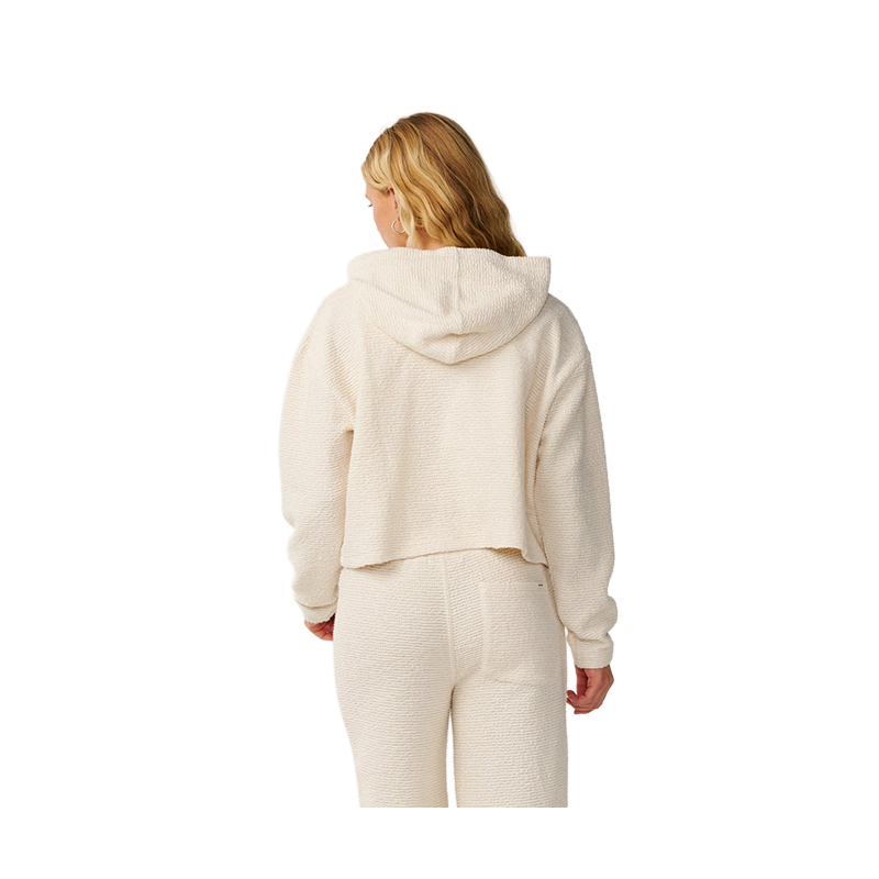 A woman viewed from the back wearing a cream-colored textured cropped hoodie and matching jogger pants against a plain white background.