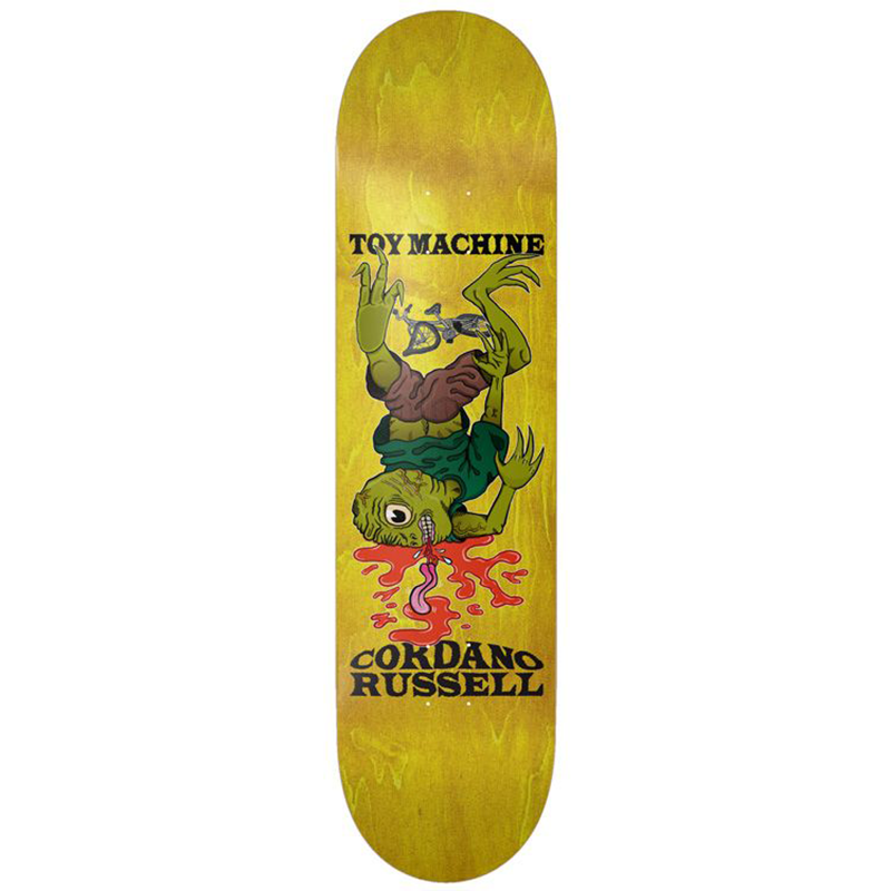 A skateboard deck featuring a yellow wood-grain finish with a graphic of a green alien-like character falling into red liquid, with the text 'TOY MACHINE' and 'CORDANO RUSSELL' printed in black.