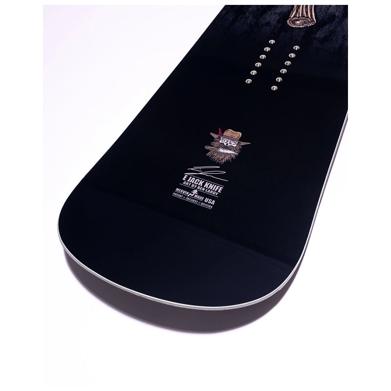 A close-up of a snowboard base showing the black wood grain, binding holes, and a Jackknife brand logo near the tail, set against a plain white background.