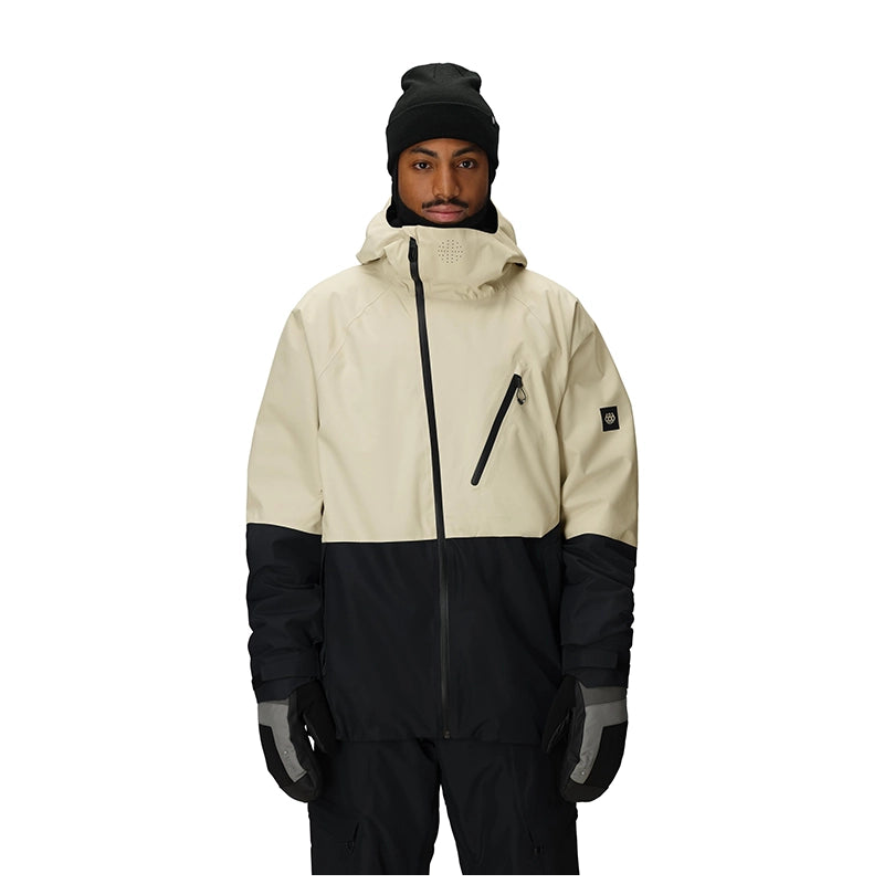 A man wearing a colorblock snowboard jacket in off-white and black, paired with a black beanie, black gloves, and black snow pants, photographed against a solid white background.