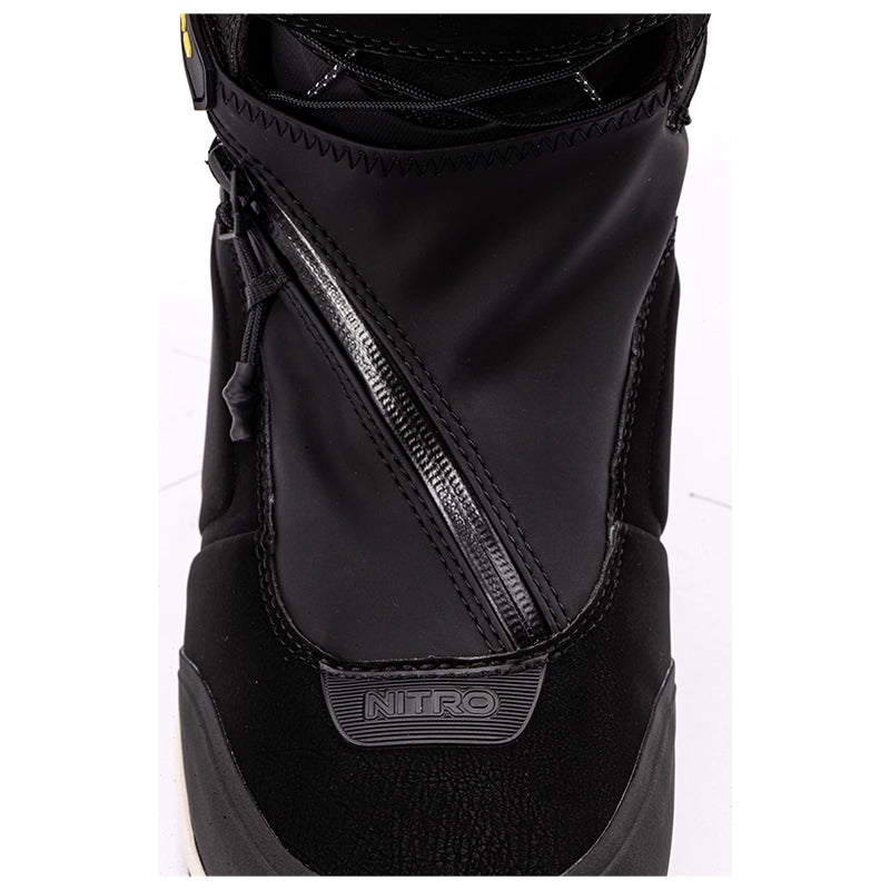 A close-up of a black snowboard boot featuring a diagonal zipper, textured synthetic leather panels, and a 'NITRO' logo badge on the toe area.