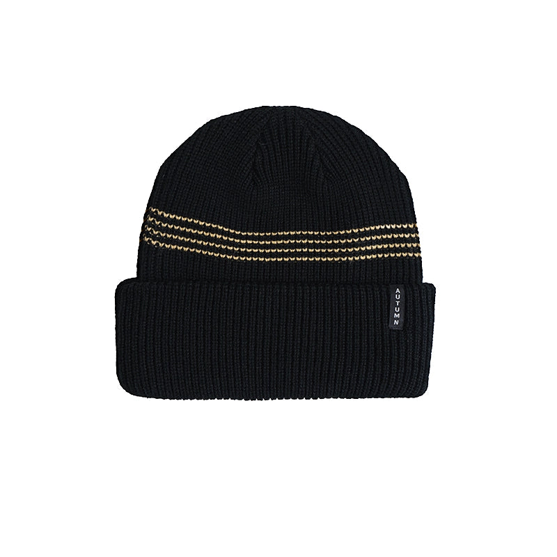 A black ribbed knit beanie hat with three horizontal gold dotted stripes across the upper portion and a small black brand tag on the folded cuff, shown against a plain white background.