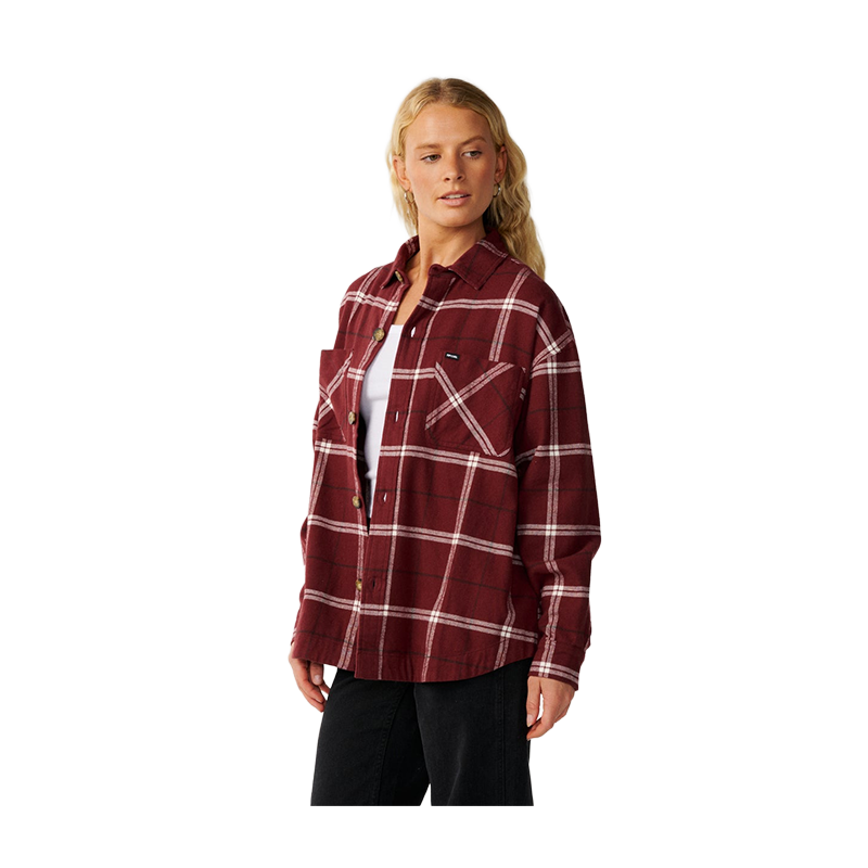A woman modeling a burgundy red plaid flannel shirt with white stripes, worn open over a white undershirt and black pants, against a solid white background.