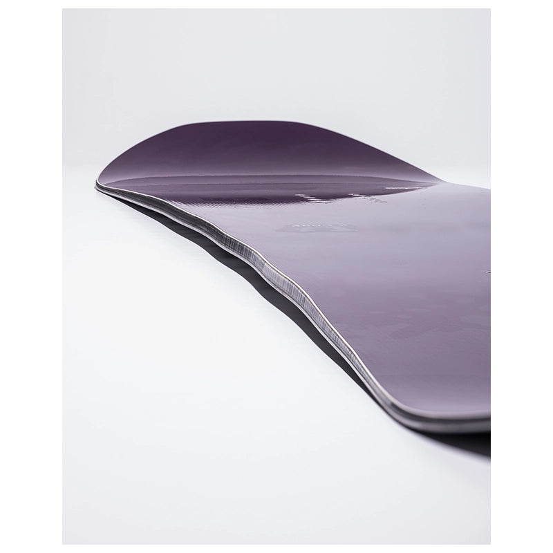 A close-up studio shot of a snowboard deck showing its purple base and the silver edge tape along the curved bottom edge, set against a clean white background.