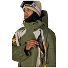 A man wearing an olive green ski jacket with cream and yellow panels, a black neck gaiter, and a beige knit beanie with ski goggles, shown against a plain white background.