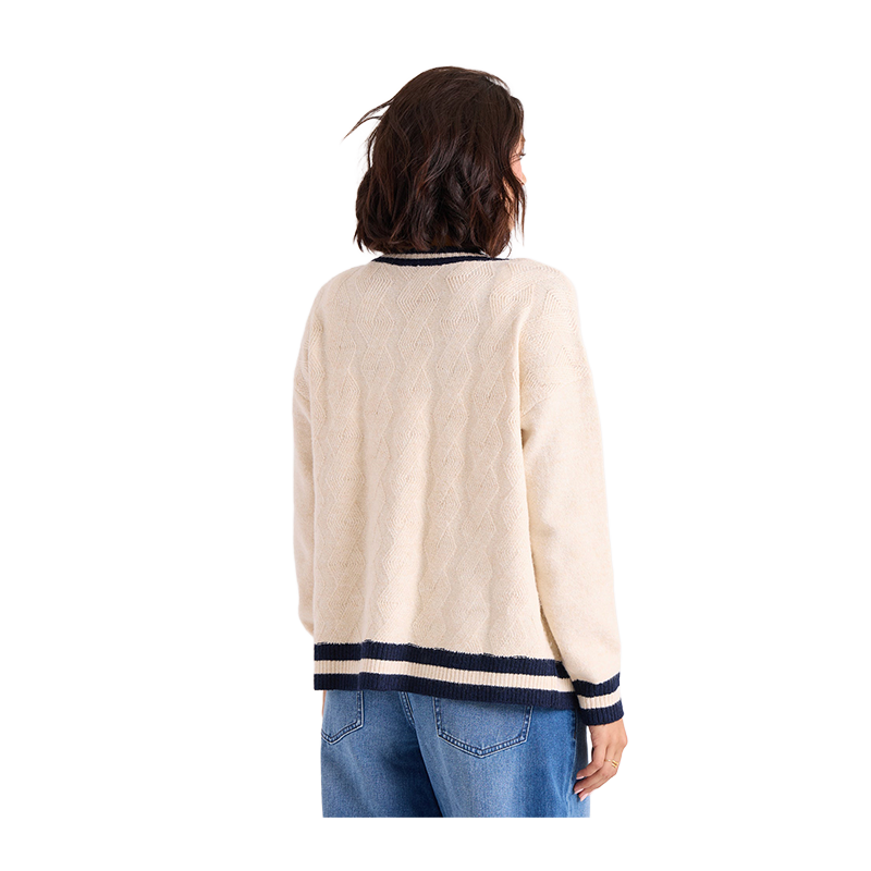 A woman shown from the back wearing a cream-colored cable-knit sweater with navy and cream striped trim at the collar, cuffs, and hem, paired with blue jeans against a plain white background.