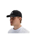 A man in profile wearing a black baseball cap with a small square logo patch on the front, paired with a white t-shirt against a light gray background.