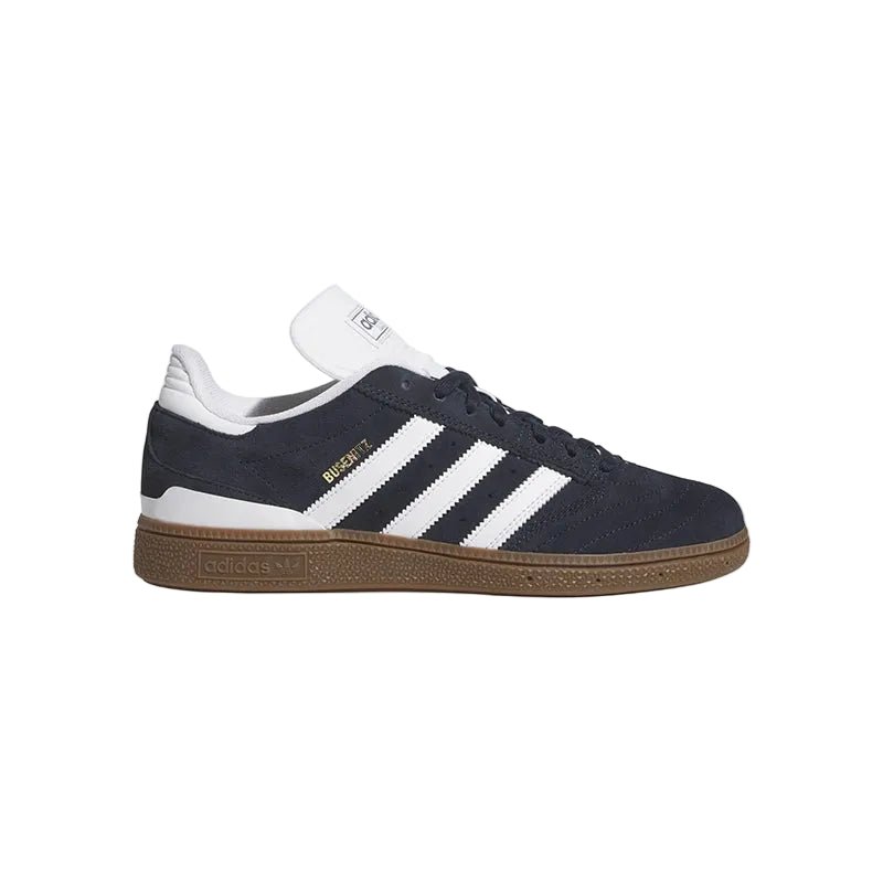 Adidas Busenitz sneaker in navy blue suede with white stripes, a white tongue, and a brown gum sole, shown against a light gray background.