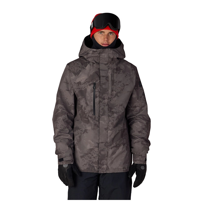 A man wearing a dark gray and black camouflage ski jacket, black snow pants, black gloves, and a red and black beanie with goggles, photographed against a solid white background.