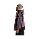 A man in profile wearing a two-tone purple and black hooded jacket, a beige knit beanie with ear flaps, and a patterned neck gaiter, standing against a plain white background.