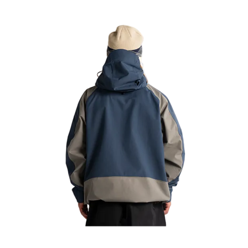 A person shown from the back wearing a color-blocked hooded jacket in navy blue, gray, and beige, paired with black pants against a plain white studio background.