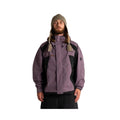 A man wearing a purple and black ski jacket, a patterned knit beanie, and black pants, standing against a plain white studio background.
