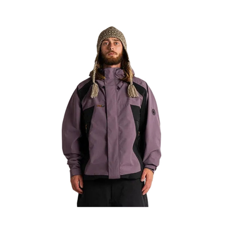 A man wearing a purple and black ski jacket, a patterned knit beanie, and black pants, standing against a plain white studio background.