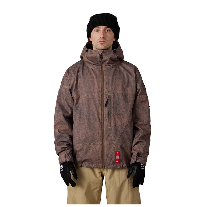 A man wearing a brown camouflage-patterned hooded snow jacket, black beanie, black gloves, and tan pants, standing against a solid white background.
