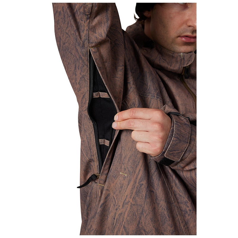 Close-up of a man wearing a brown camouflage-patterned jacket, opening a side zipper to reveal a black inner lining, against a plain white background.