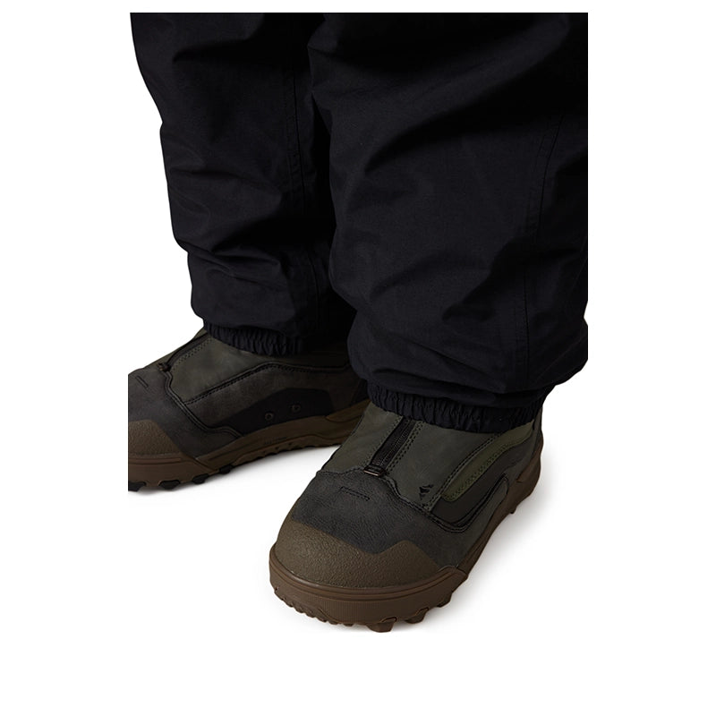 Close-up of a person's lower legs wearing dark navy pants and dark olive-brown waterproof boots with elastic cuffs, shown against a plain white background.