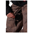 Close-up of a person wearing brown and black patterned snowboard pants, showing a hand opening a side pocket.