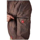 Close-up of a brown textured jacket with a hand pulling a black zipper on the sleeve pocket, featuring a small red brand patch.