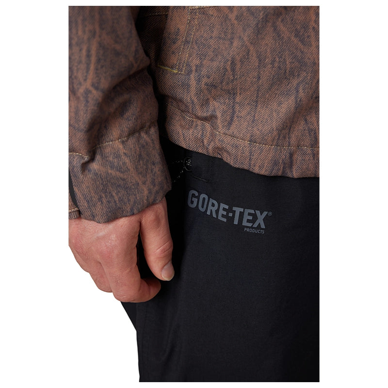 Close-up of a person wearing a brown patterned jacket and black pants with a visible GORE-TEX logo on the thigh.