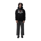 A model stands against a solid white background wearing a black hoodie with a white and red graphic print on the chest, paired with black and gray pinstriped trousers and black shoes.