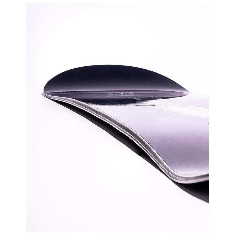 A close-up studio shot of a curved snowboard showing the dark black top sheet and the light lavender-purple underside, with a clean white background.