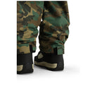 Close-up of camouflage snow pants with black and tan snowboard boots, shown from the back against a white background.