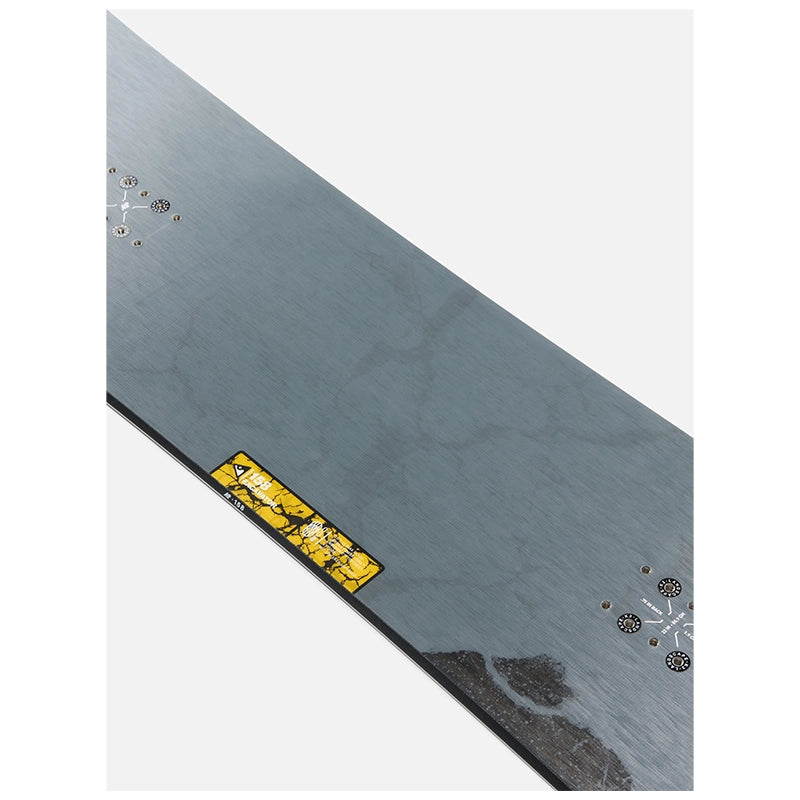 A close-up of a dark gray metal surface, likely a skateboard deck underside, showing printed snowflake graphics, mounting holes, and a small yellow warning label.
