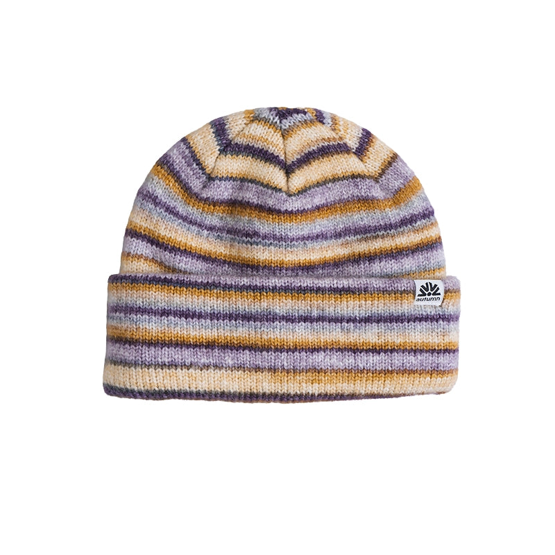 A knit beanie hat with horizontal stripes in purple, mustard yellow, and cream, featuring a small white embroidered logo patch on the folded cuff.