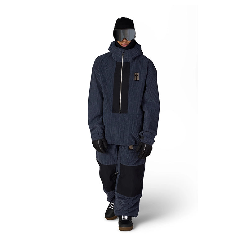 A model wearing a dark navy blue snowboard jacket with a black front panel, black snow pants, a black beanie, and goggles, standing against a plain white background.