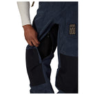 Close-up of a person wearing dark navy corduroy pants with black knee patches and a gold embroidered logo on the thigh, shown against a white background.