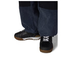 A close-up of a person's feet wearing dark navy blue corduroy trousers and black work boots with brown soles, shown against a plain white background.