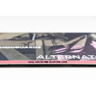 A close-up of a printed item, likely a book, magazine, or album cover, showing partial text including 'SNOWBOARDS', 'ALTERNATIVE', and 'HAUL ASS GO BIG GLAM ONE LOVE' on a mostly black, white, and pink cover.