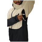 A close-up of a person wearing a colorblock ski jacket with a cream upper section and a dark navy lower section, showing the adjustable hood and zippered chest pocket.