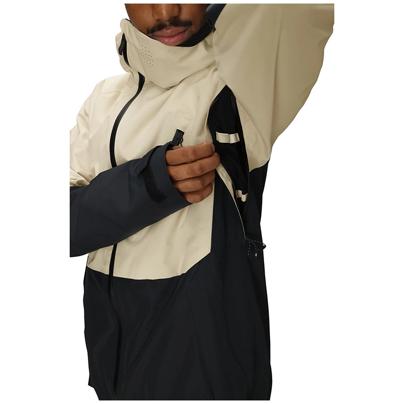 A close-up of a person wearing a colorblock ski jacket with a cream upper section and a dark navy lower section, showing the adjustable hood and zippered chest pocket.