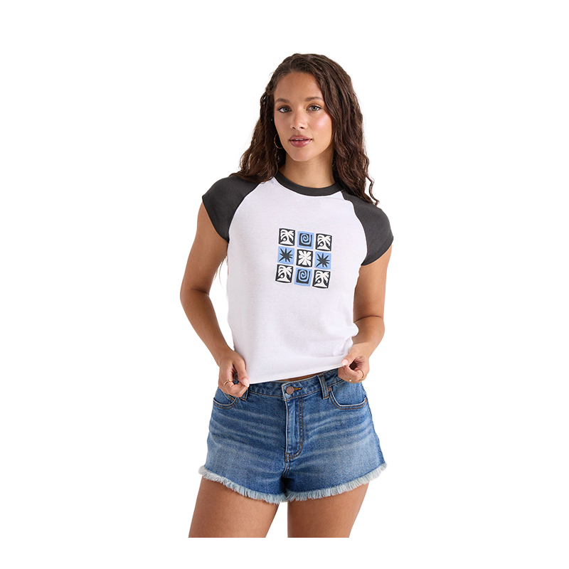 A woman modeling a white raglan t-shirt with dark gray sleeves and collar, featuring a blue graphic print on the chest, paired with denim shorts against a plain white background.
