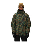A man wearing a camouflage winter jacket, tan knit beanie, and black gloves, standing against a solid white background.