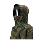 A person wearing a hooded camouflage jacket and black ski goggles, shown in profile against a plain white background.
