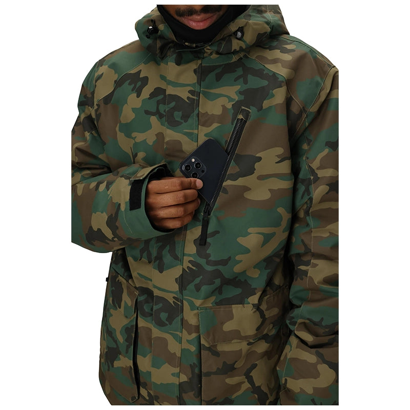 A person wearing a hooded camouflage jacket, holding a black smartphone in one hand. The jacket features a green, brown, and black woodland camo pattern, and the photo is cropped from the chin down against a plain white background.