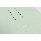 A close-up of a light mint green snowboard with white printed graphics, including a logo reading 'FOREVER SNOWMACHINE' and alignment hole markings.