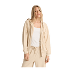 A woman modeling a light beige zip-up hoodie and matching sweatpants over a white ribbed tank top, photographed against a solid white background.