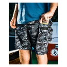 Person wearing camouflage shorts with a blue shirt, standing in front of a blurred background.