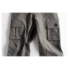 Close-up of dark gray cargo pants showing the right leg with a large flap cargo pocket and a circular black logo patch on the pocket flap, set against a plain white background.