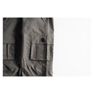Close-up of dark gray cargo pants showing the side pocket with a snap-button flap and the main body fabric, set against a plain white background.