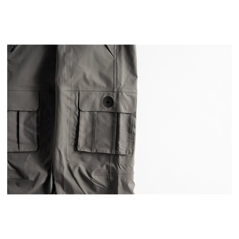Close-up of dark gray cargo pants showing the side pocket with a snap-button flap and the main body fabric, set against a plain white background.