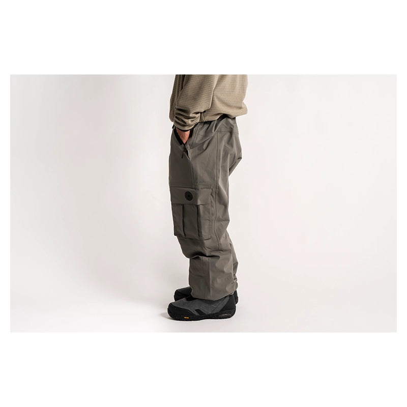 A person shown from the waist down wearing gray cargo pants, a beige long-sleeve top, and black snowboard boots against a plain white studio background.