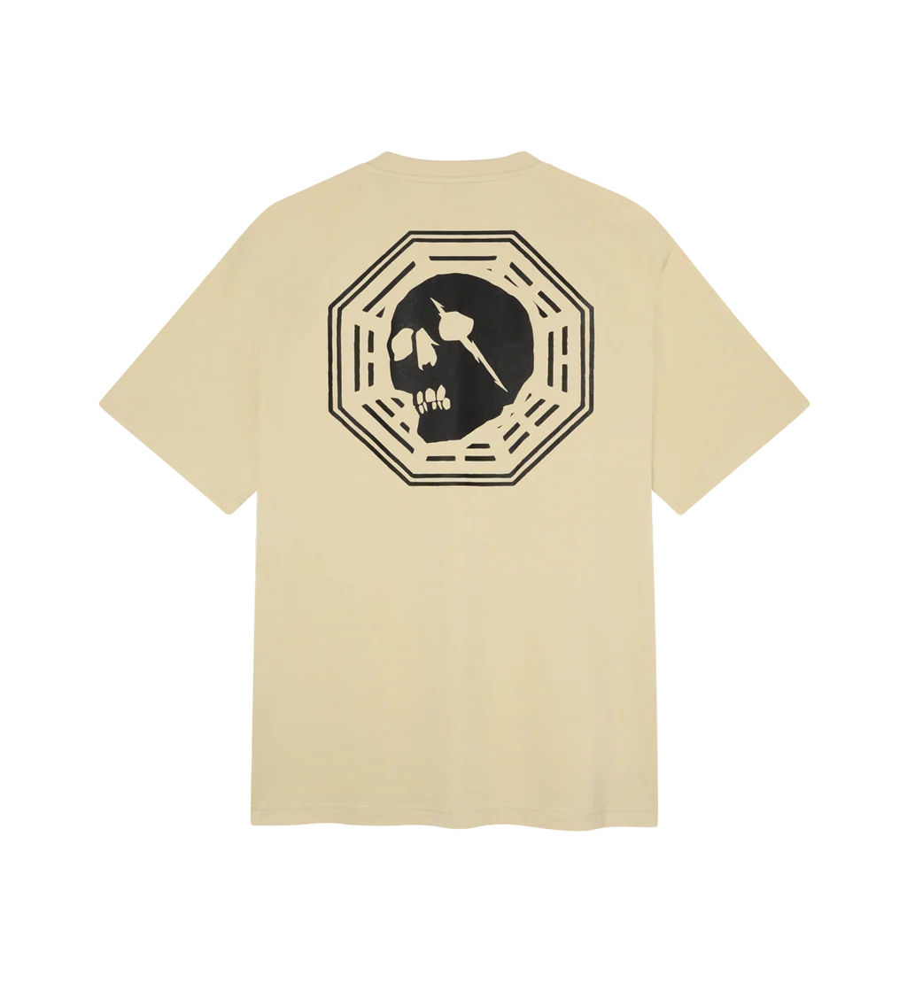 A beige short-sleeve t-shirt shown from the back, featuring a large black graphic of a skull inside an octagonal frame.